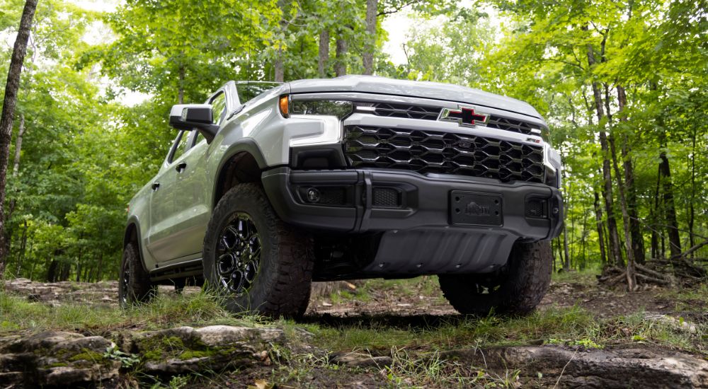 A low angle view of a white 2024 Chevy Silverado 1500 ZR2 parked off-road in a forest.