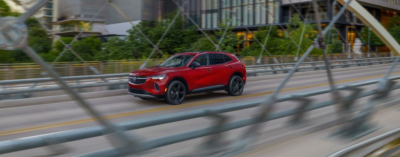 A red 2023 Buick Envision is shown driving over a city bridge.