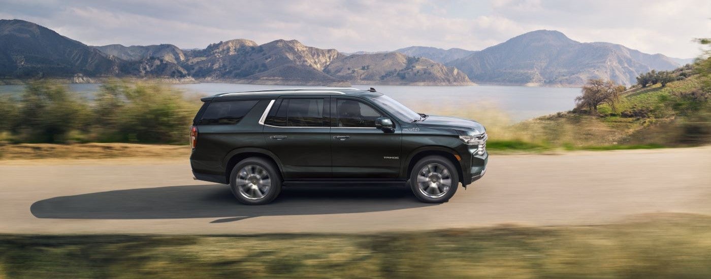 A dark grey 2022 Chevy Tahoe High Country is shown driving past a lake after leaving a Chevy dealer.