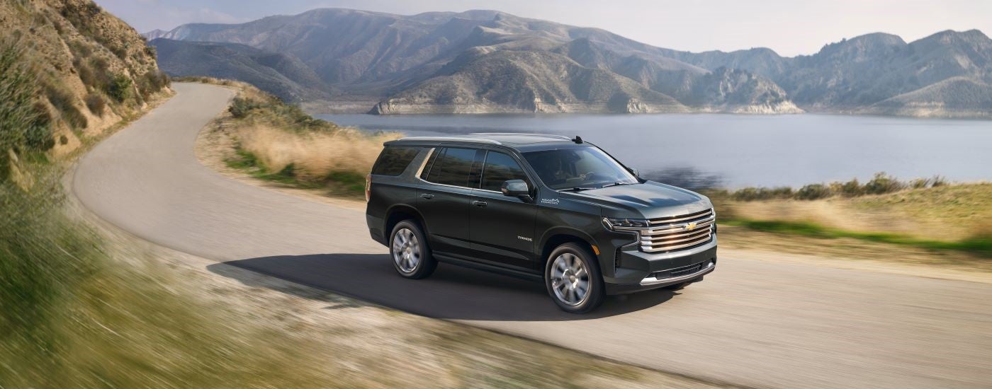 A dark grey 2022 Chevy Tahoe High Country is shown driving past mountains after visiting a used Chevy dealer.
