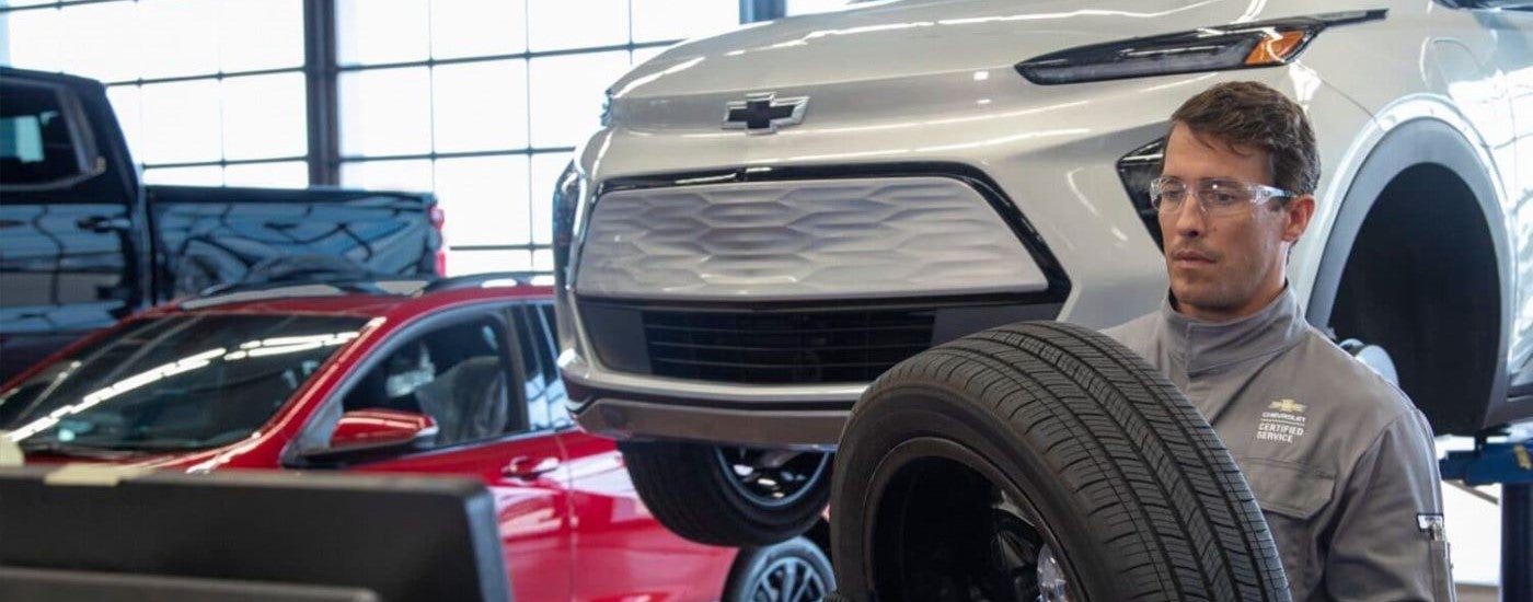 A mechanic is shown changing the tire on a silver 2023 Chevy Bolt EUV on a lift.