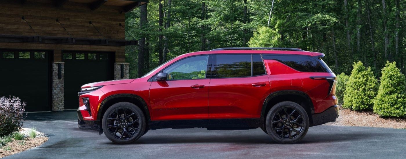Side view of a red 2024 Chevy Traverse RS parked in a rural driveway.