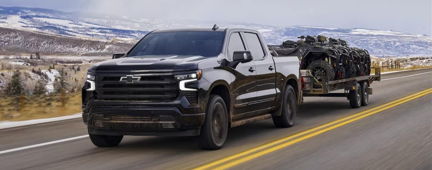 A black 2024 Chevy Silverado 1500 High Country towing a trailer with ATVs.
