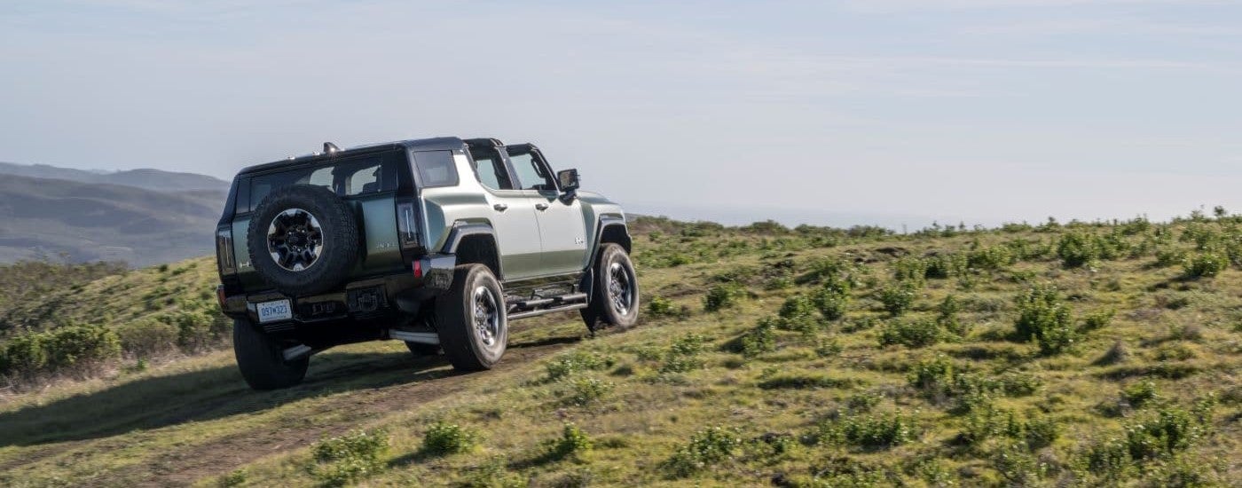 A green 2024 GMC Hummer EV is shown driving on grass.